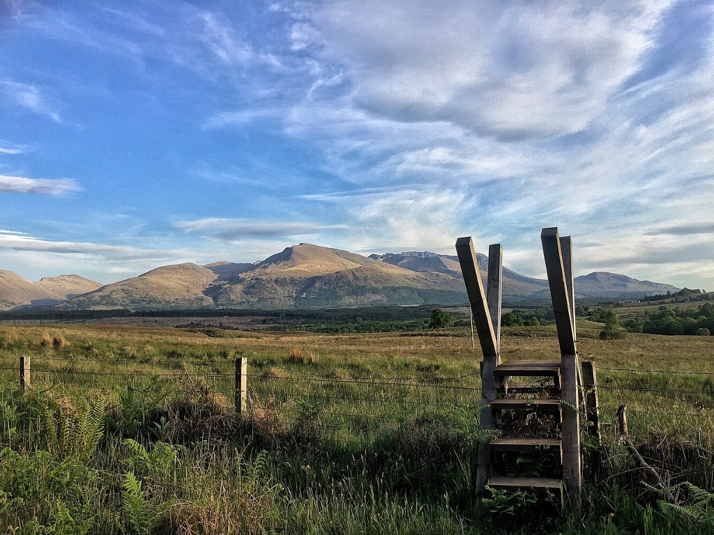 Wooden stile over a fence, with a mountain in the background.