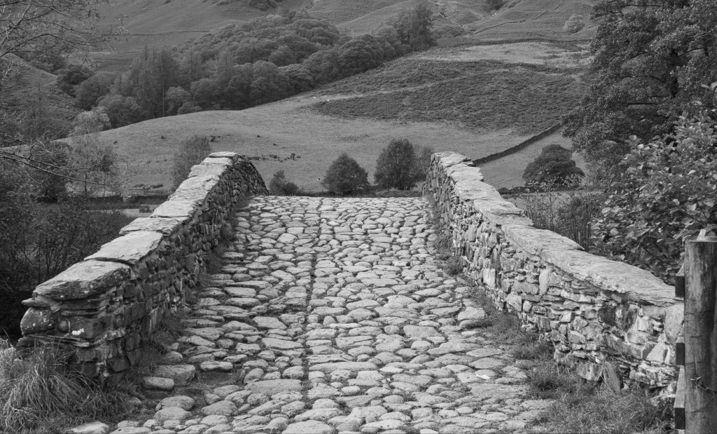 Black and white image of an old stone packhorse bridge.