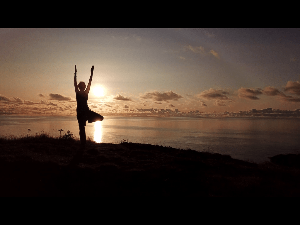 Figure of a woman in a yoga pose in front of the setting sun