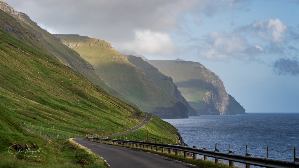 A winding coastal road, with mountains to the left and the sea to the right.