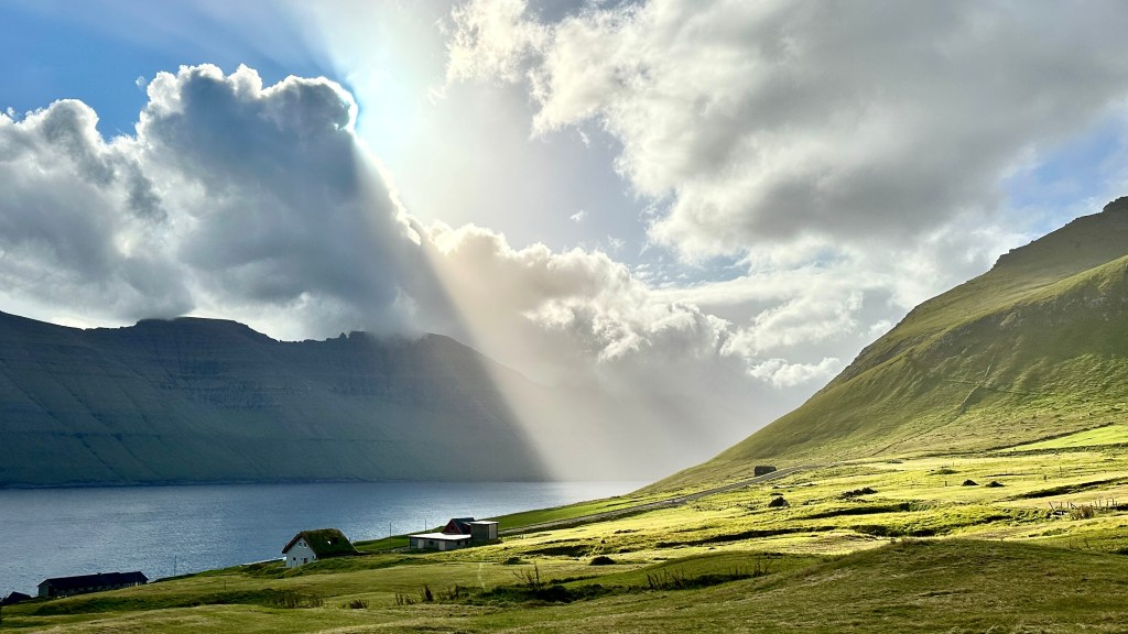 A grassy hillside, with sunlight lighting up half the sky and hillside, with the other half in shade.