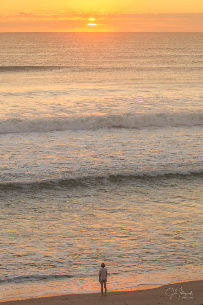 Lone female stood in front of an ocean at sunrise