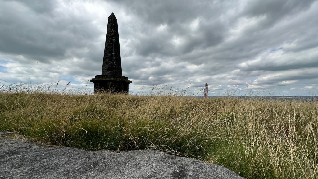 Stoodley Pike with a very small figure looking up at it to the right.