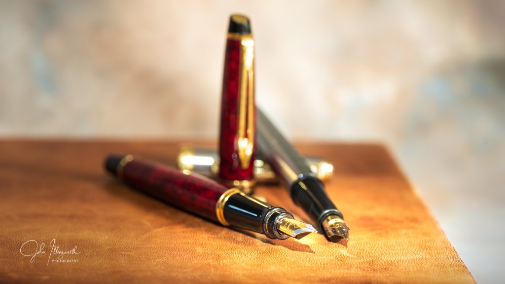 two fountain pens, one tortoise shell and one stainless steel, laid on a leather bound book, with nibs side by side. 