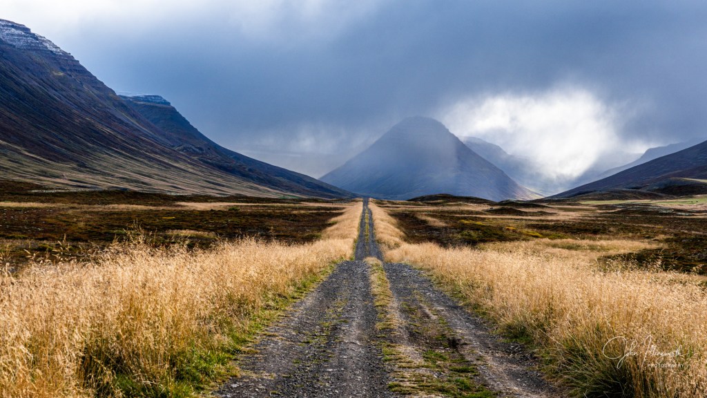 an unpaved dirt road stretching into the distance, towards a mountain in the background.