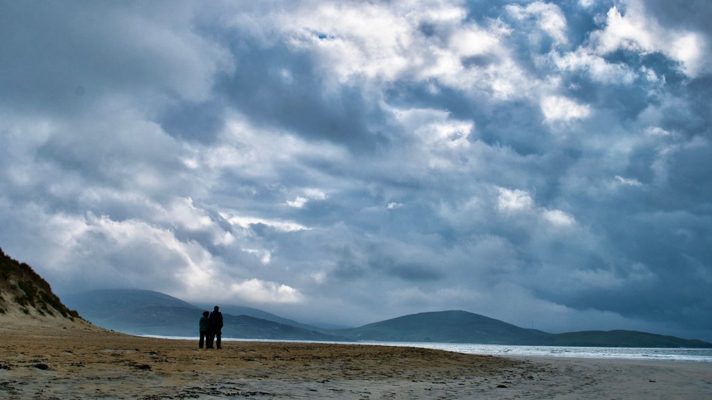 two people stood side by side looking out to sea under a cloudy sky