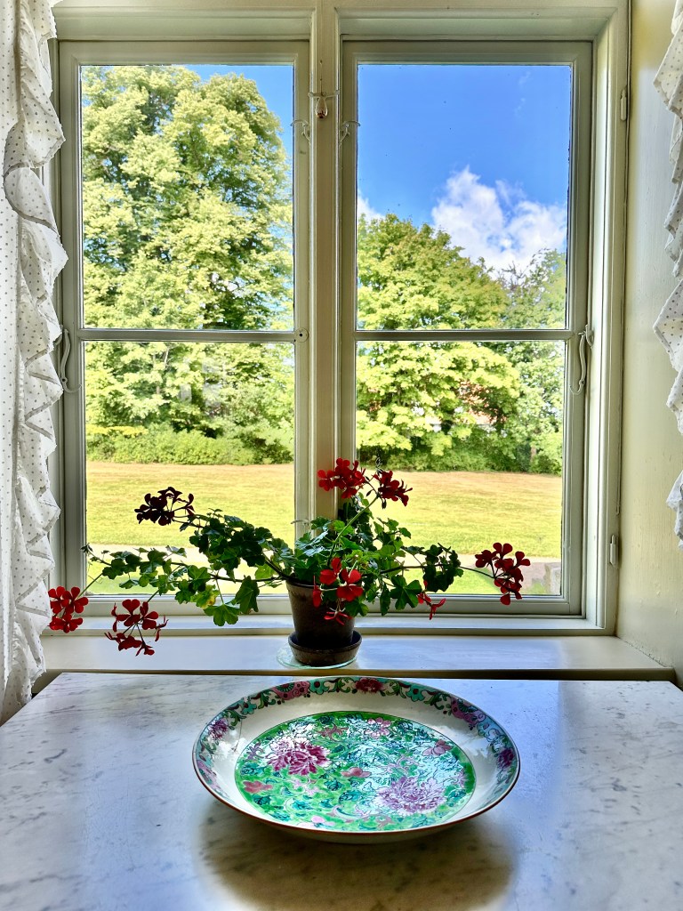 Vase of flowers in front of a window looking out to a garden at Rungstedlund, Denmark.