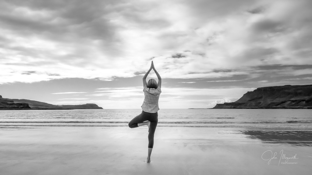 Figure with her back to the camera, facing out to sea, in a yoga pose. 