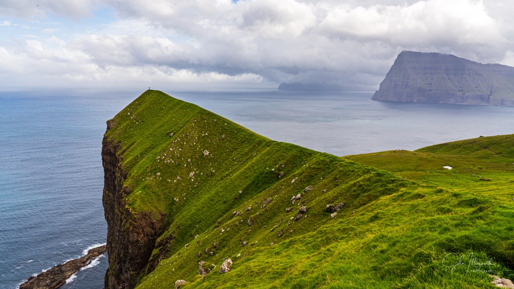 image of a coastline, with a small figure stood on the edge of a grassy buttress.